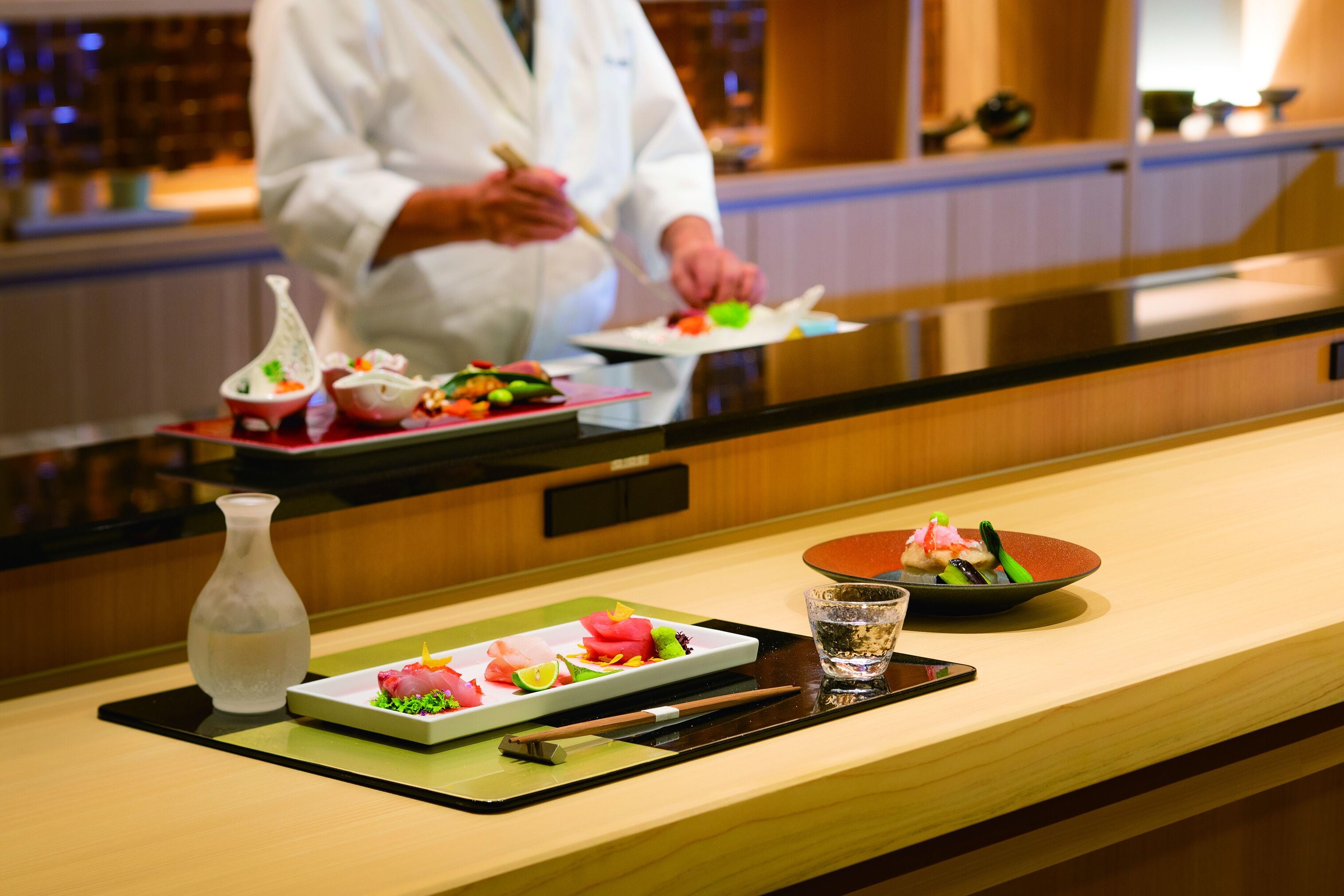 A sushi bar with a chef preparing food, a water glass, and a bottle of water on the counter.