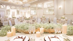 Un salón de banquetes con mesas redondas, sillas blancas, candelabros y centros de mesa florales.