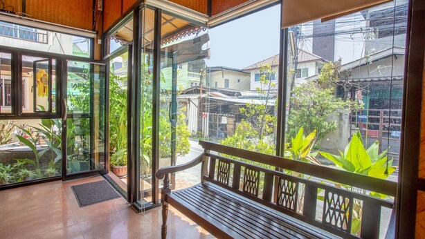 A spacious balcony with a wooden bench, large glass doors leading to a garden, and a view of the surrounding neighborhood. - Le Viengping (Chiang Mai)