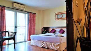 A hotel room with a bed, a chair, a window with curtains, and a wall-mounted air conditioner. - Pangviman Place Resotel (Chiang Mai)