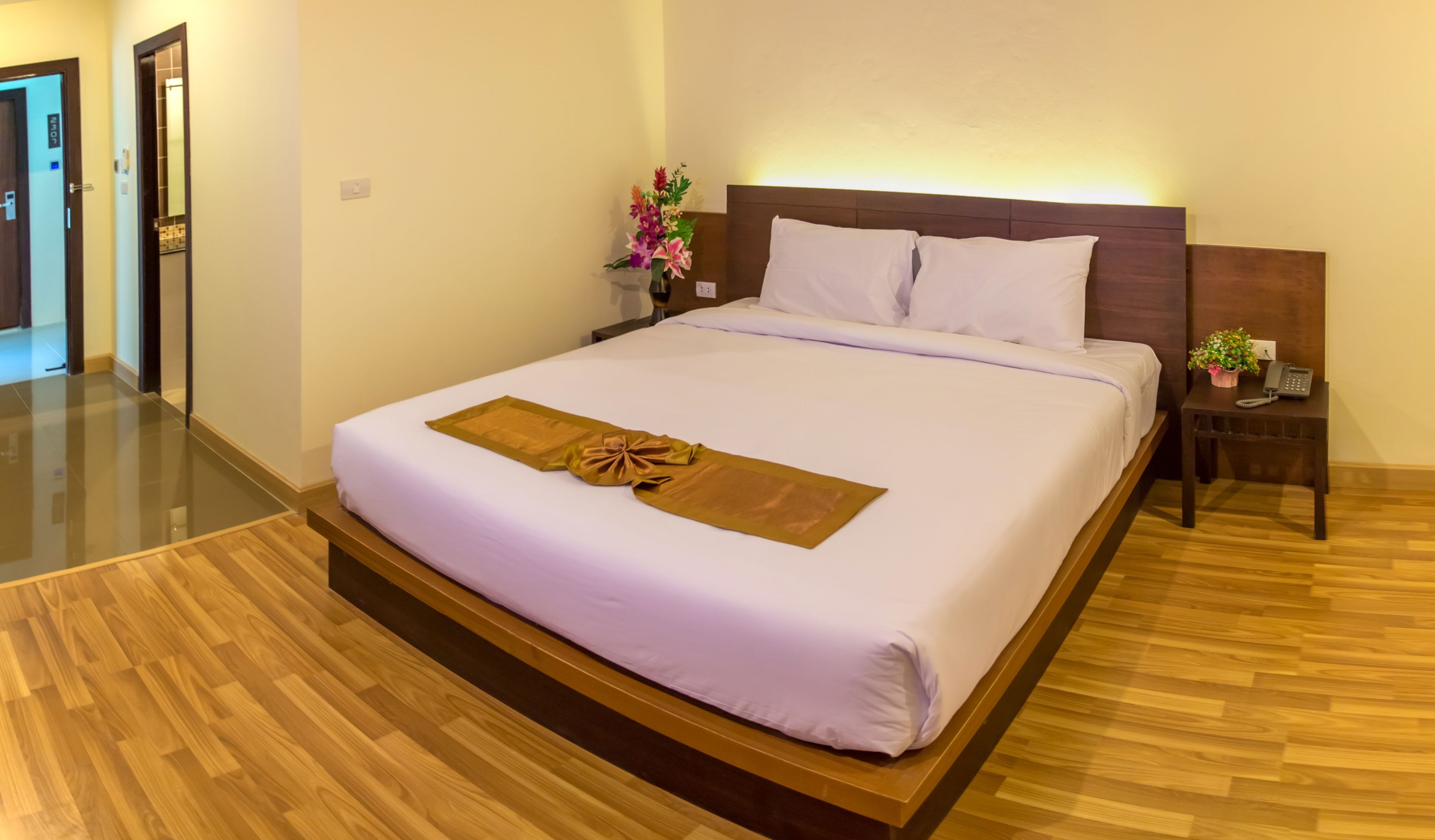 A hotel room with a large bed, wooden floor, a nightstand with a phone, and a vase with flowers.