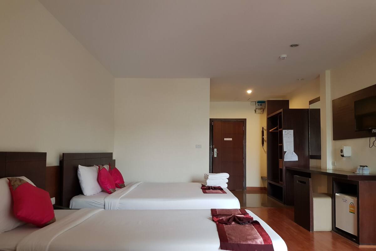 A hotel room with two beds, a desk, a TV, and a minibar.