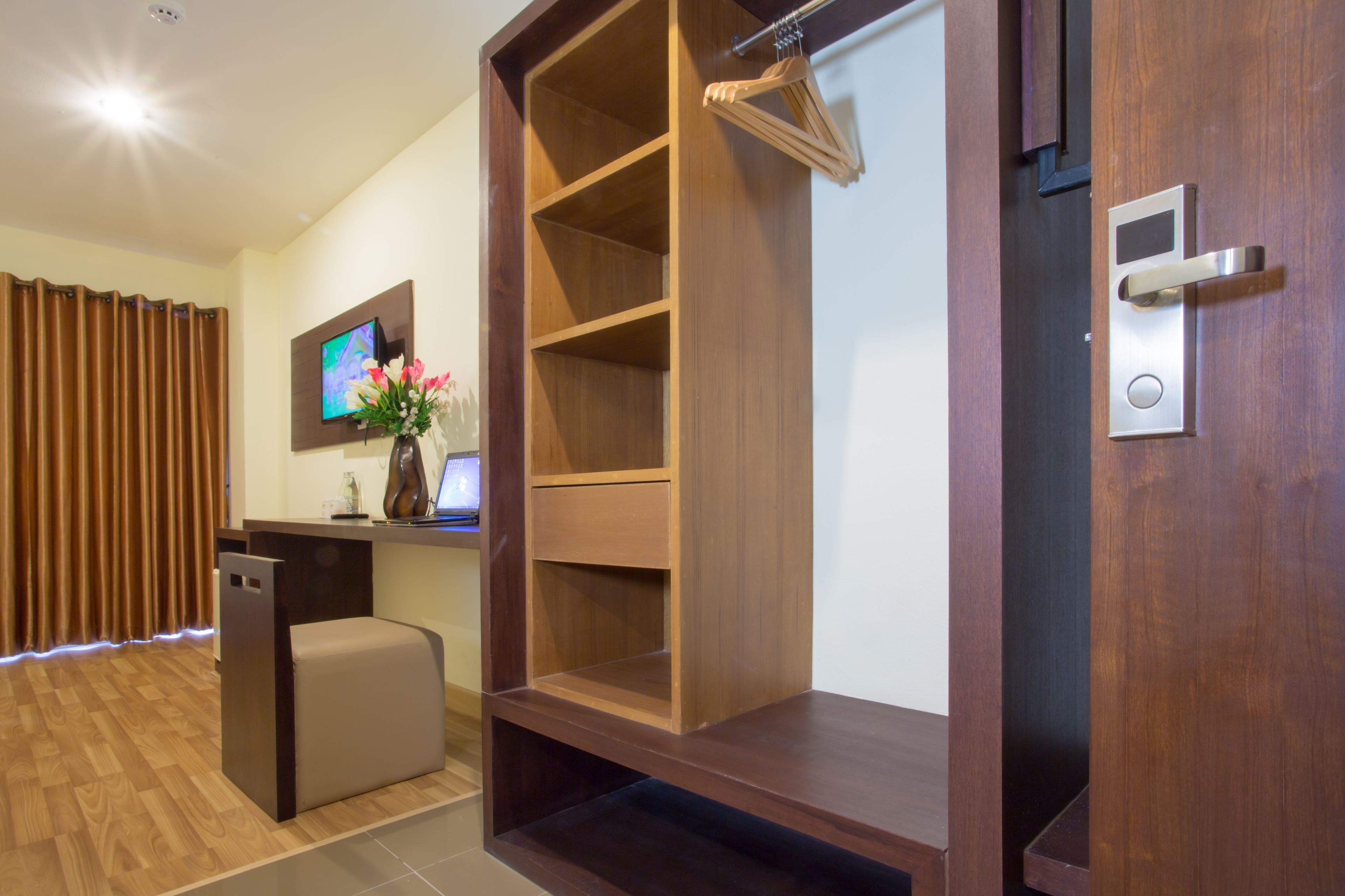 A modern hotel room with a wooden reception desk, a television, a small seating area, and a wardrobe with hanging space.