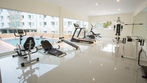 A modern gym with various exercise equipment, large windows, and a view of a building complex. - Pangviman Place Resotel (Chiang Mai)