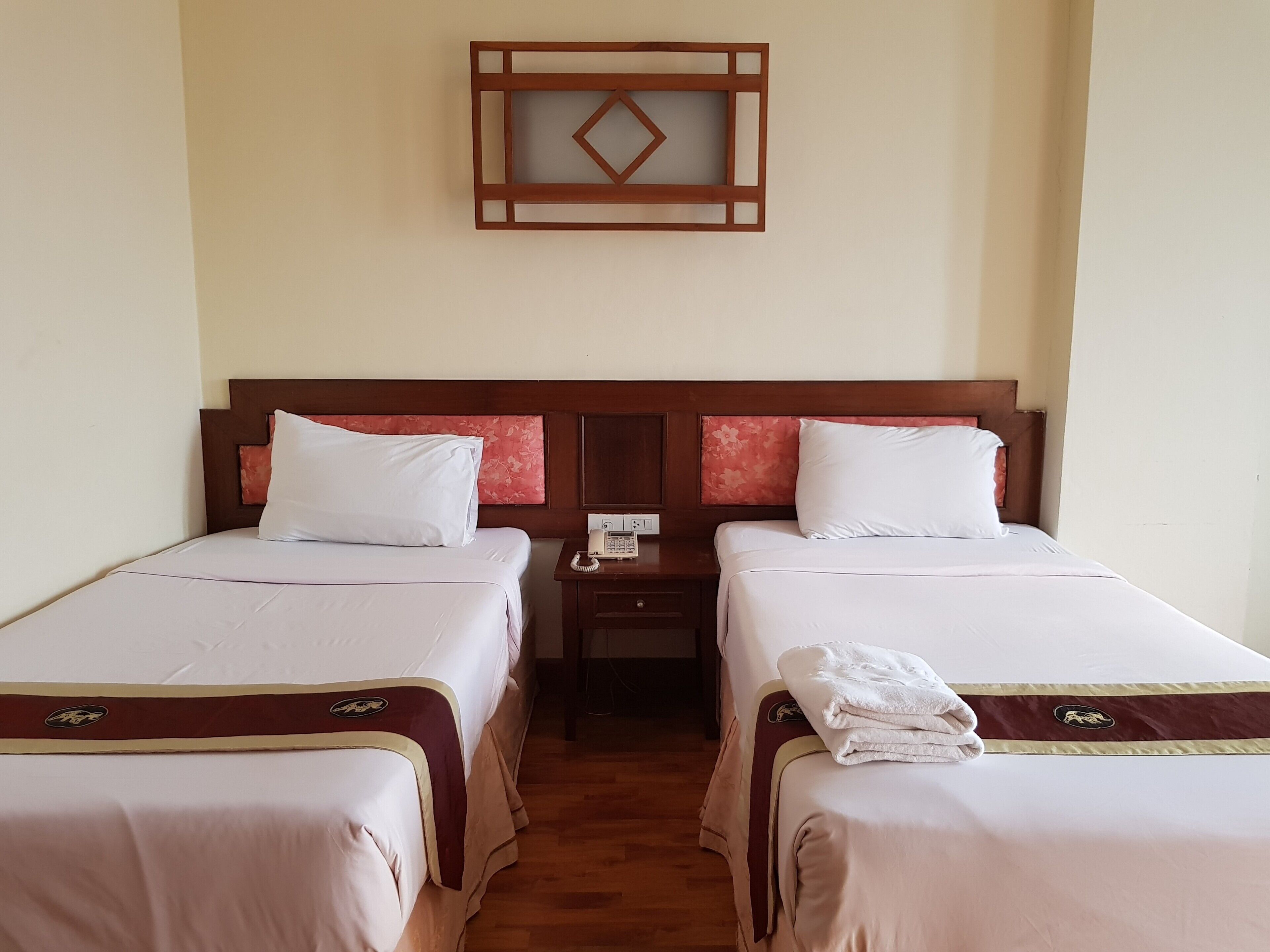 Ein Hotelzimmer mit zwei Einzelbetten, jeweils mit einem Holzkopfstück, weißer Bettwäsche und einem kleinen Nachttisch mit Telefon.
