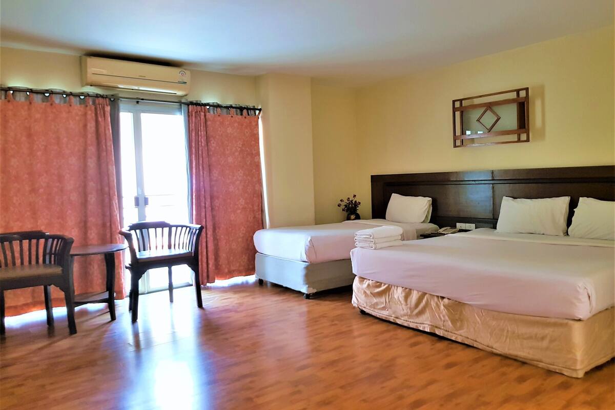 A hotel room with two beds, a desk with chairs, and a window with curtains.