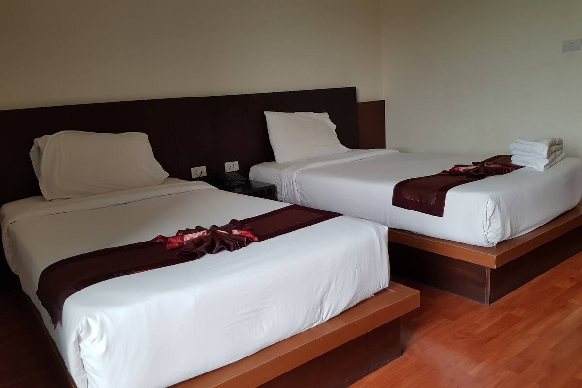 Two single beds with wooden headboards, white linens, and a red decorative runner.