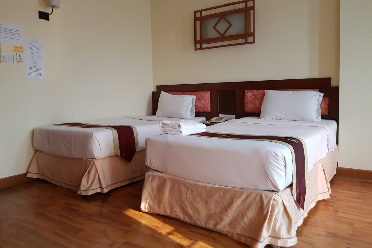 A hotel room with two beds, wooden flooring, a wall-mounted light fixture, and a framed picture.
