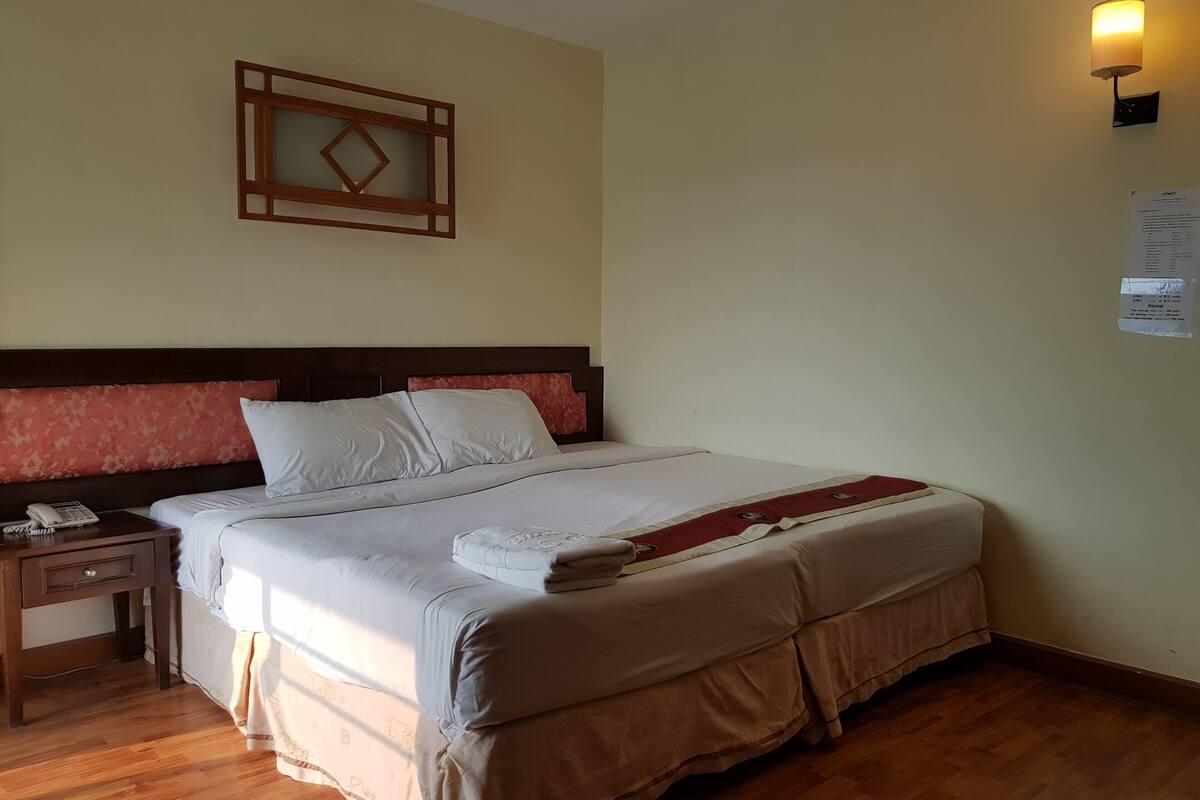 A neatly made bed with white linens, a wooden nightstand with a telephone, and a wall-mounted light fixture.