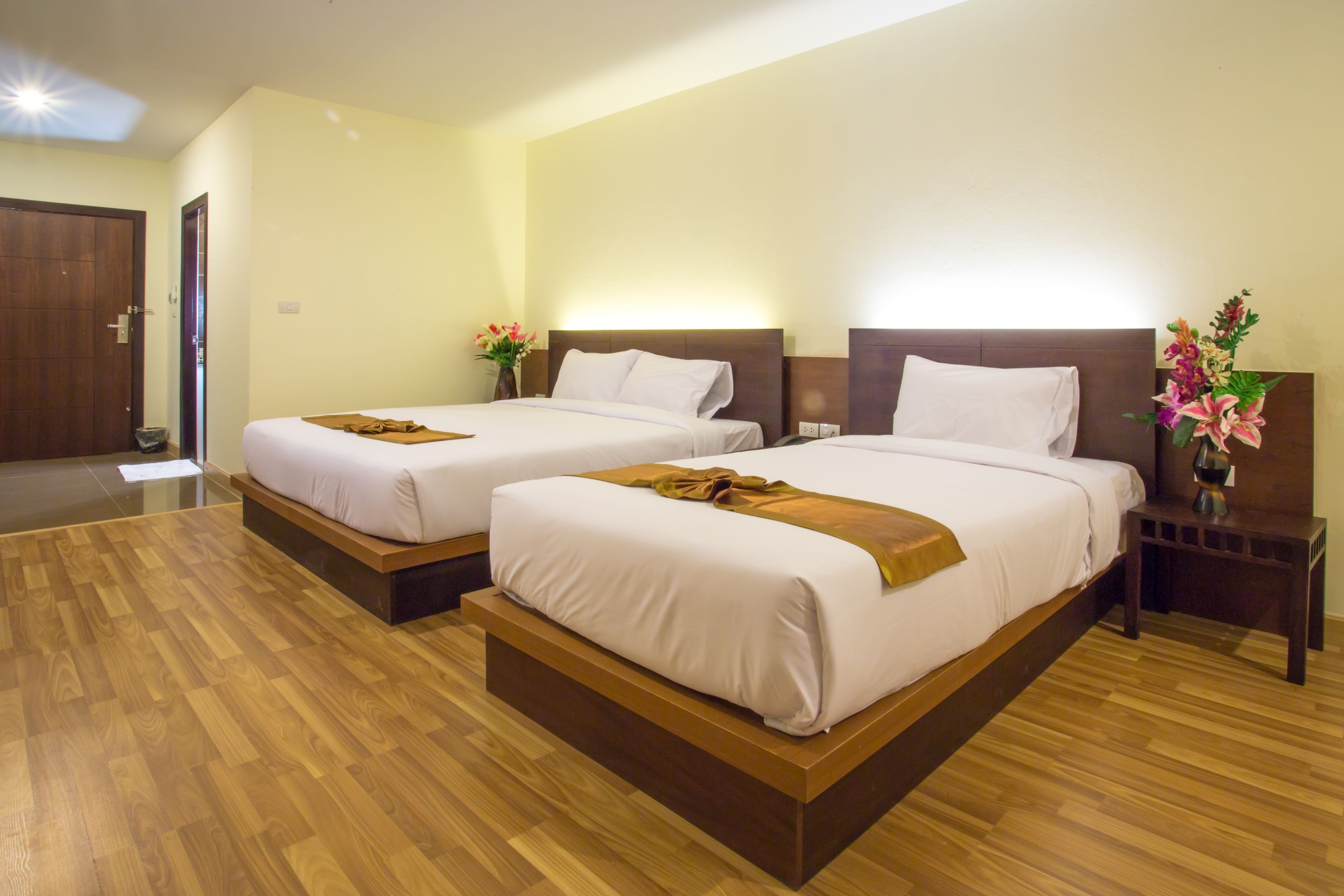 A hotel room with two beds, wooden flooring, and a nightstand with a vase of flowers.