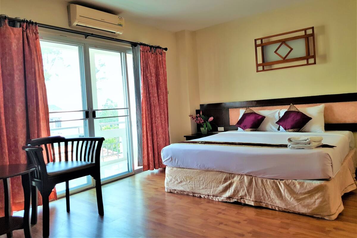 A hotel room with a bed, a chair, a nightstand, and a window with curtains.
