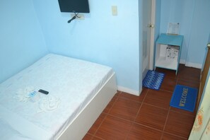 A small, single-bed room with a blue wall, a bedside table with a power outlet, a remote control, and a welcome mat. - The Beach Anne Boracay (Boracay Island)