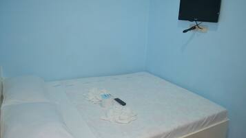 Una habitación pequeña con una cama individual, pared azul lisa, televisor montado y ropa de cama y toallas blancas.