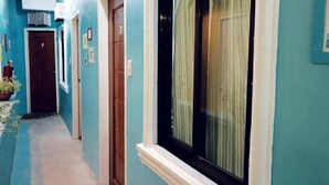 A narrow hallway with blue walls, a wooden door, and a window with a white frame and green curtains.