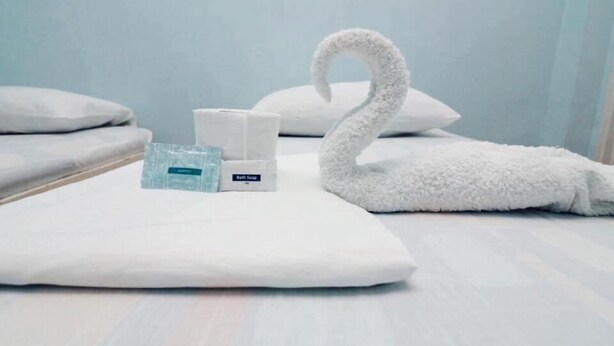A neatly made bed with a white swan-shaped towel, a bottle of bath soap, and a white pillow.