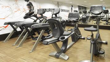 Un gimnasio con varias bicicletas estáticas y cintas de correr, suelo de madera, y una pared con arte abstracto y la palabra “DURING”.