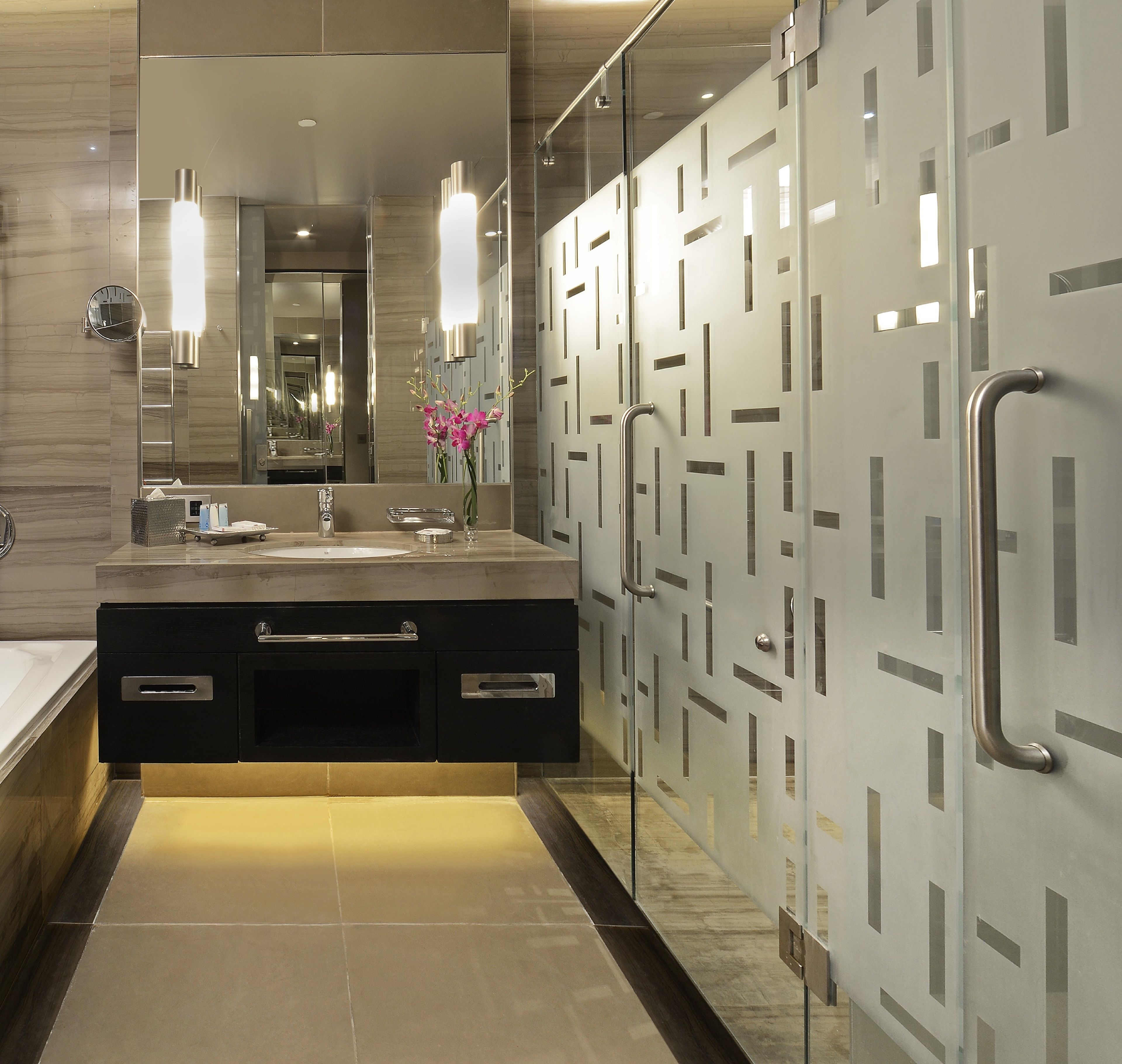 A modern bathroom with a large mirror, a sink with a vanity, and a glass partition with handles.