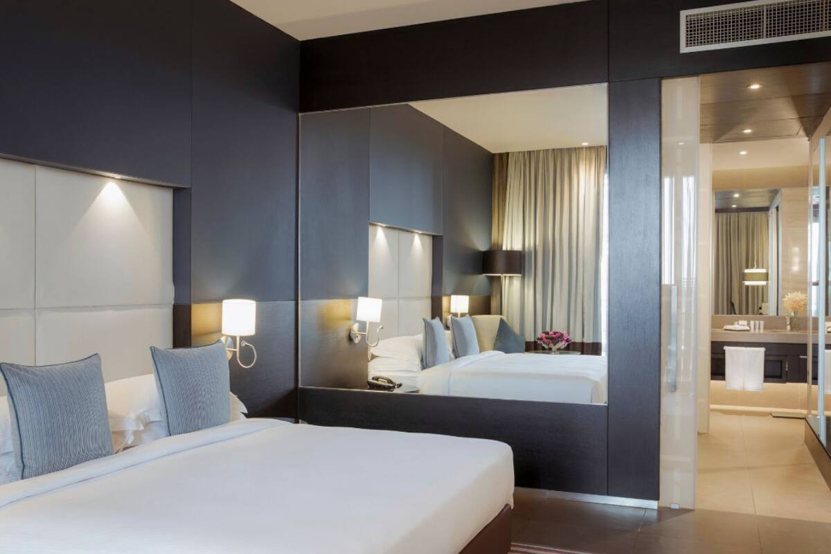 Quarto de hotel moderno com uma cama grande, um espelho e um banheiro visível por uma porta aberta.