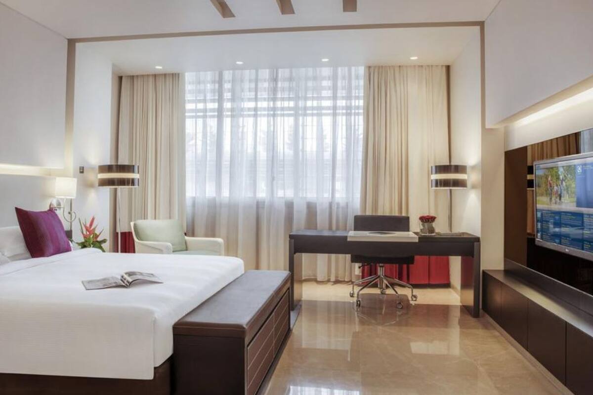 Quarto de hotel moderno com uma cama grande, uma escrivaninha, uma cadeira e uma televisão de tela plana.