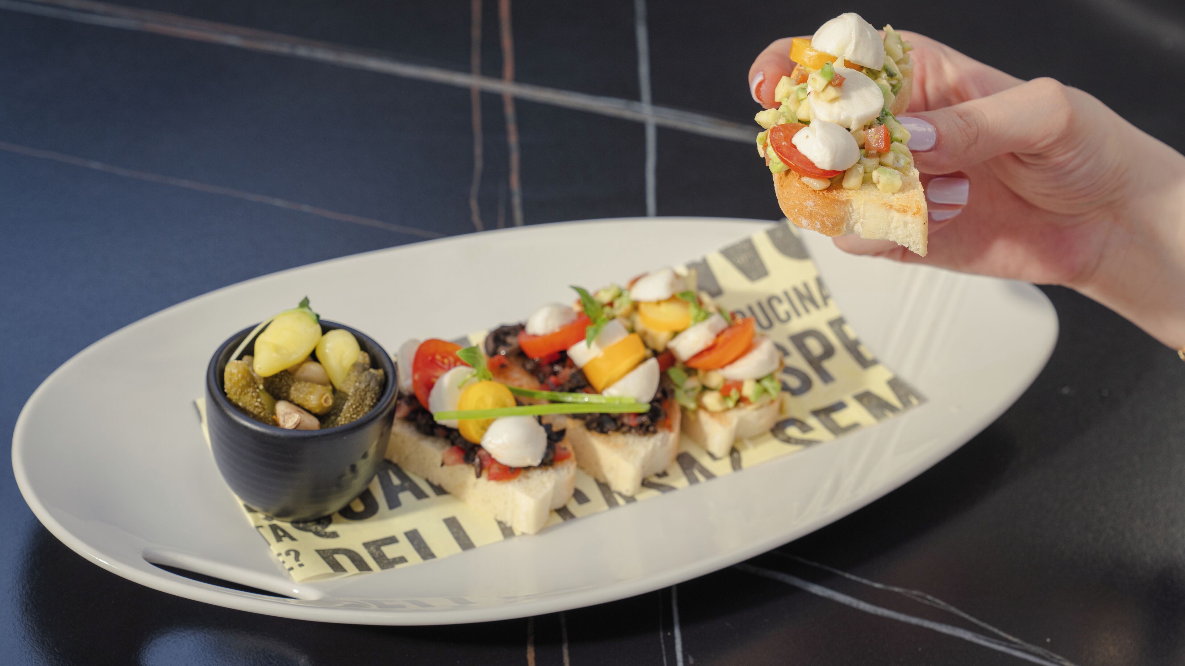 A plate with a variety of food items, including a small bowl of olives and a sandwich with vegetables and cheese.