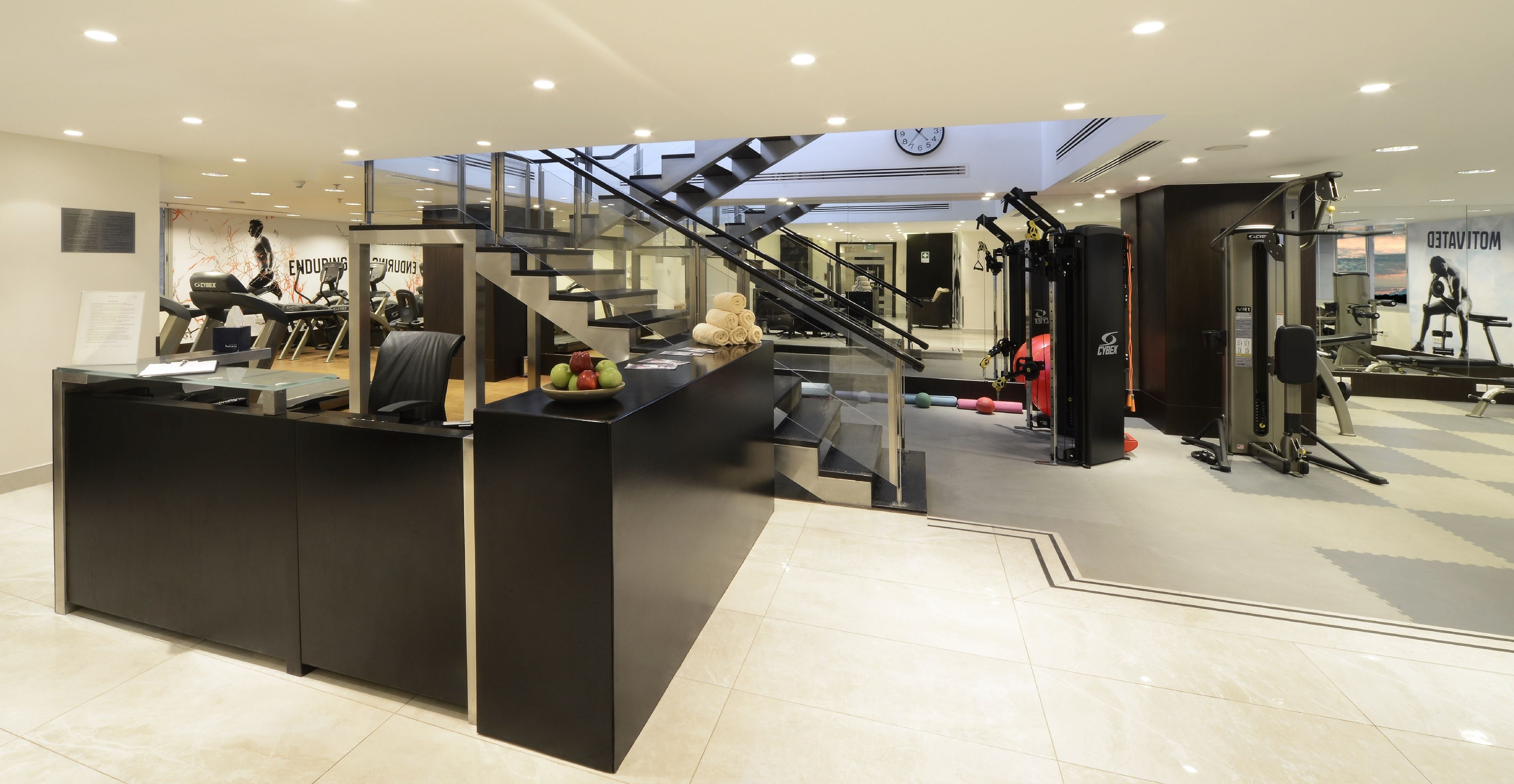A gym with a reception desk, exercise equipment, and a staircase.
