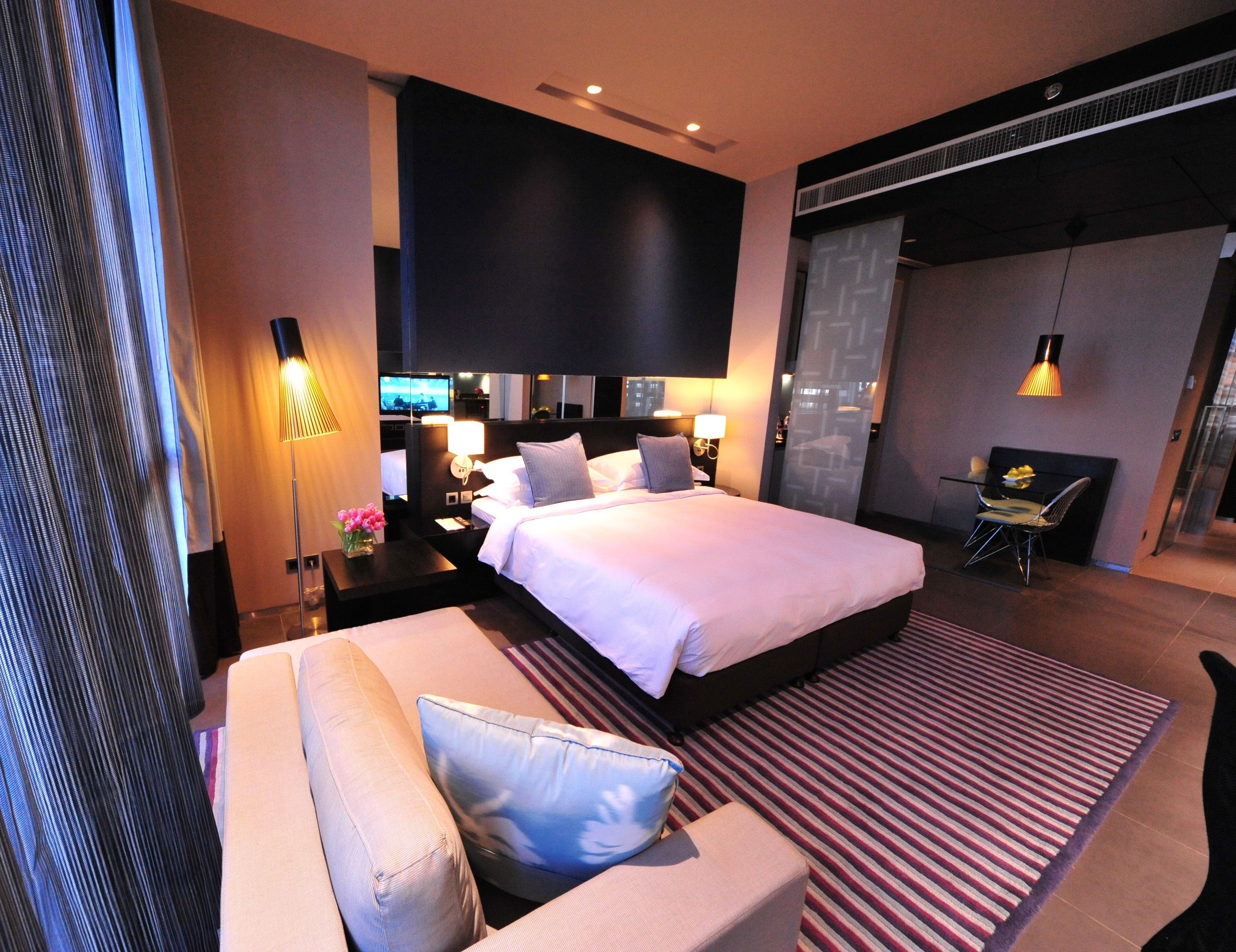 Ein modernes Hotelzimmer mit einem großen Bett, einer Couch, einem Schreibtisch mit Stuhl, einem Fernseher und einem großen Fenster.