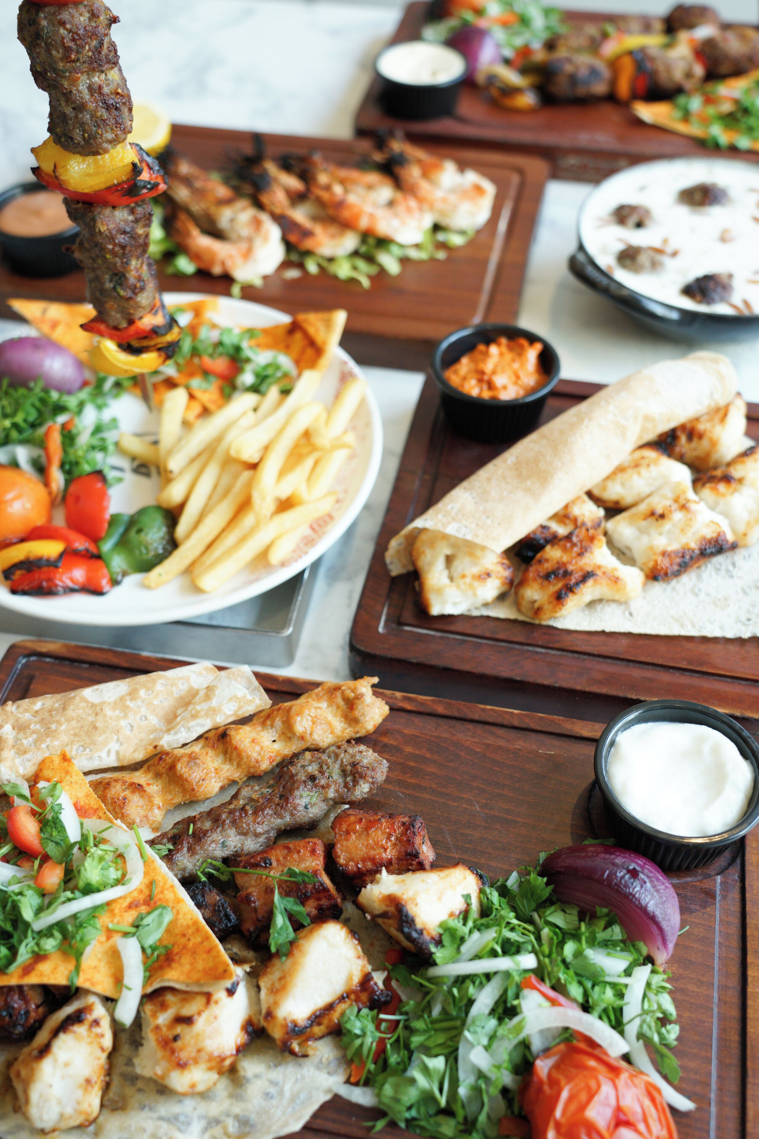 Verschiedene gegrillte Fleischsorten, Gemüse und Fladenbrote auf Holzbrettern.