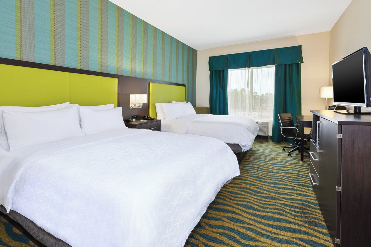 Een hotelkamer met twee bedden, een bureau met een computer, een televisie en een raam met gordijnen.