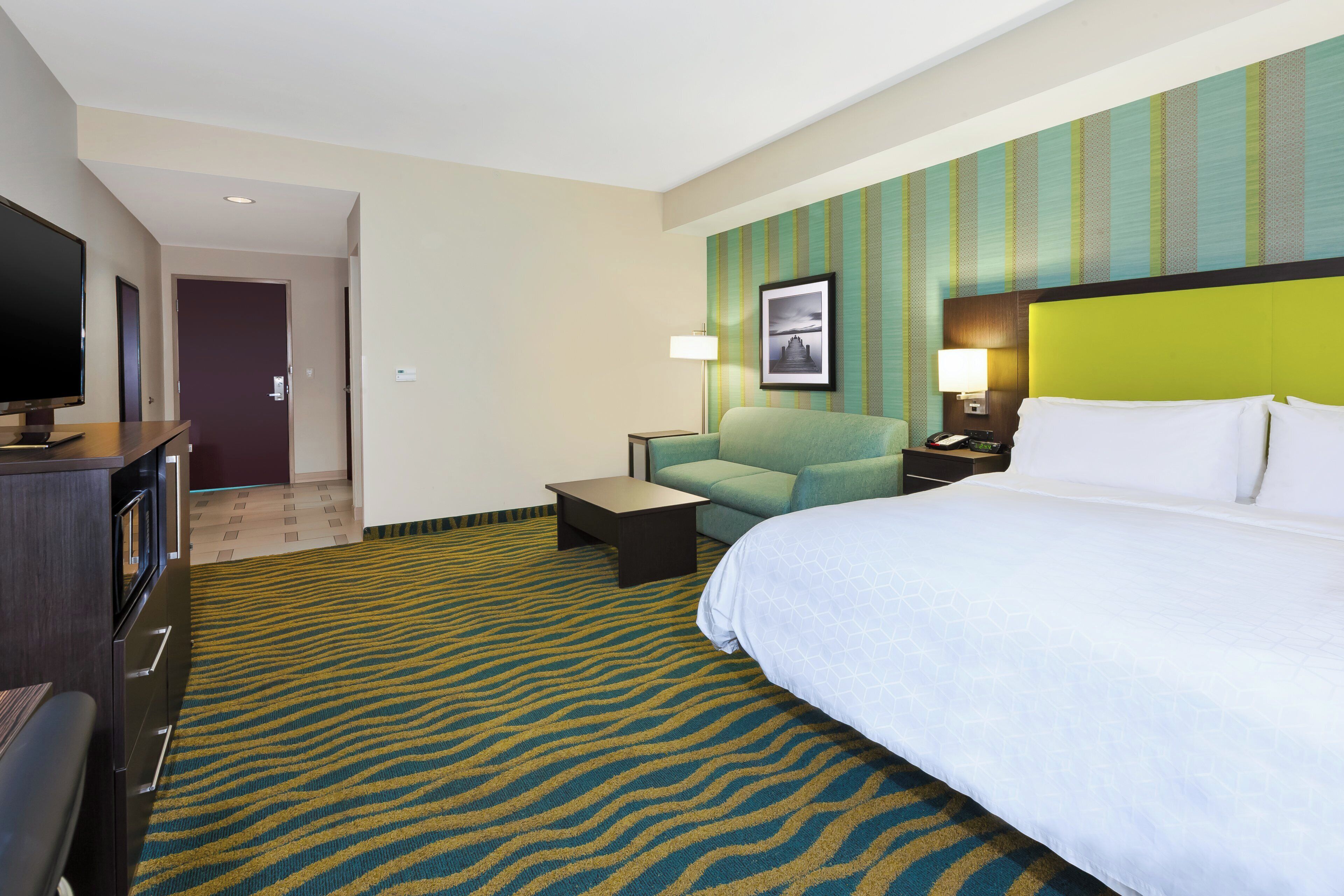 Habitación de hotel con una cama grande, un sofá, un televisor, un escritorio y una alfombra estampada.