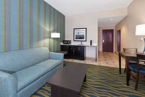 Habitación de hotel con un sofá azul, una mesita pequeña, una zona de cocina con microondas, cafetera y un cuadro en la pared.