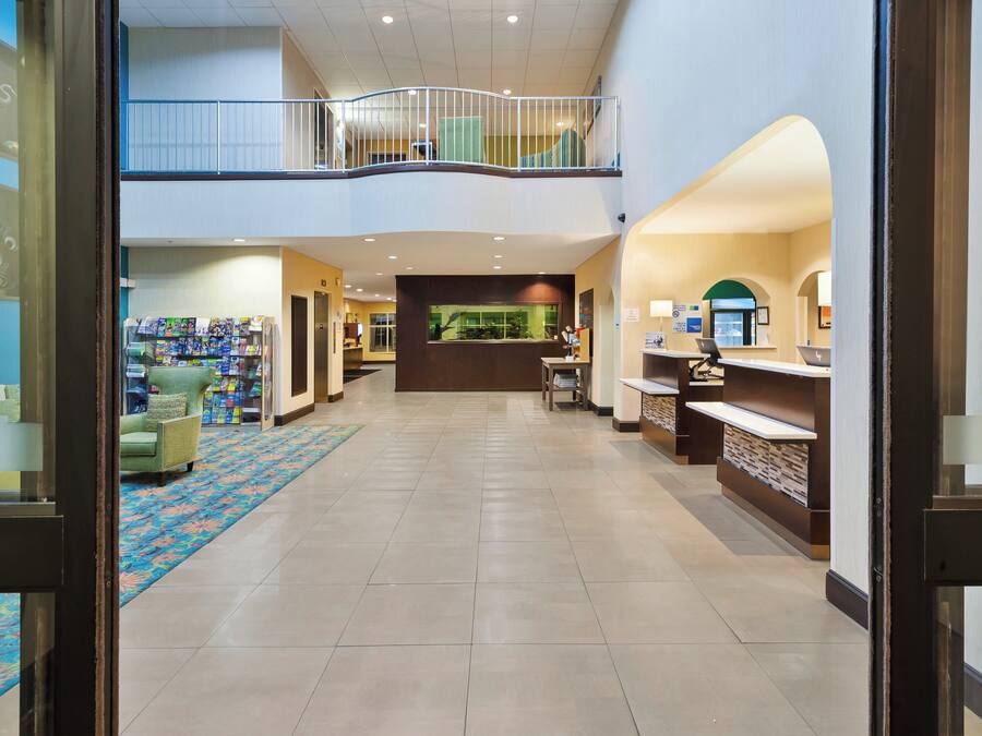 Un hall de hotel con mostrador de recepción, zona de estar y un balcón en el segundo piso.