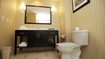 A bathroom with a sink, mirror, toilet, and a trash bin.