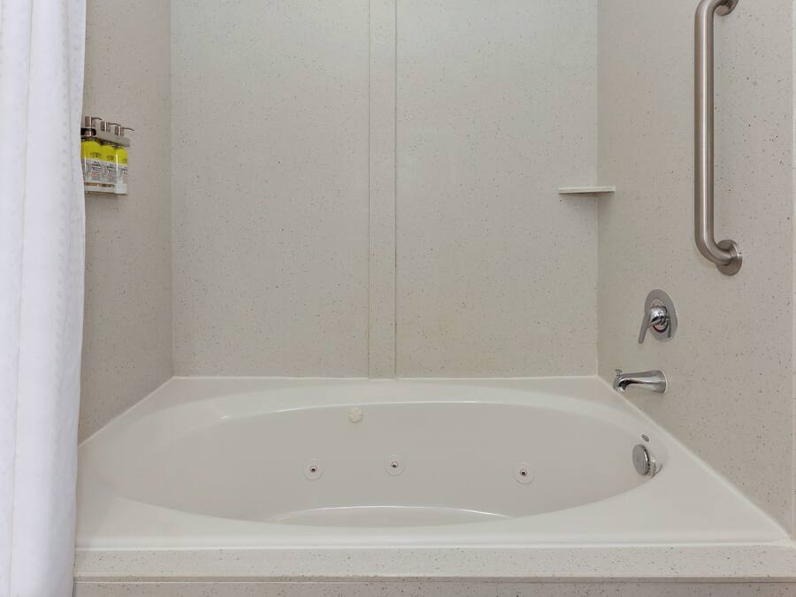 A white bathtub with a shower curtain, a handheld showerhead, and a wall-mounted faucet.