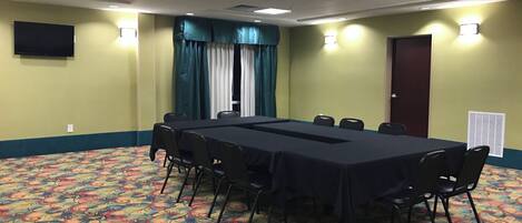 Uma sala de conferência com uma mesa comprida, cadeiras, uma televisão e carpete estampado.
