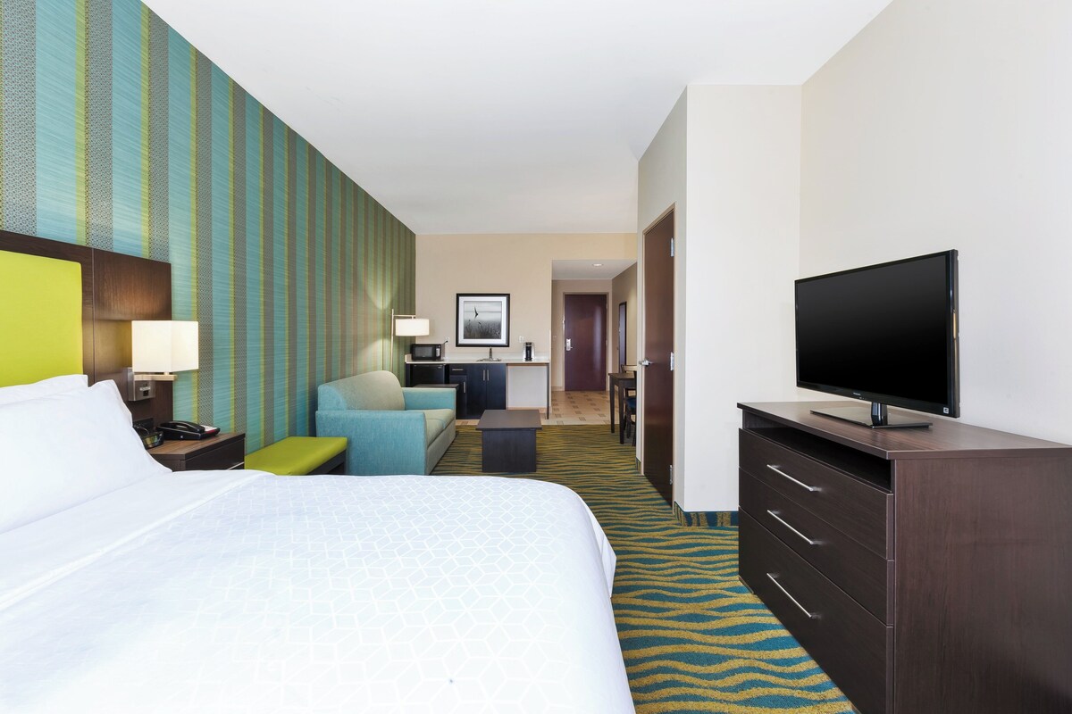 Hotelkamer met een groot bed, een televisie, een bureau met lamp, een stoel en een kleine kitchenette.