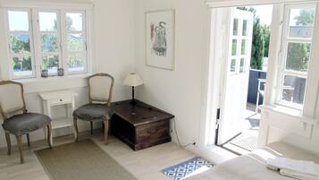 A room with two chairs, a desk, a lamp, a bed, and a window.