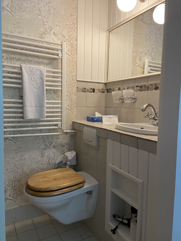 Une salle de bain comprenant des toilettes, un lavabo, un miroir, un porte-serviettes et un revêtement mural décoratif.