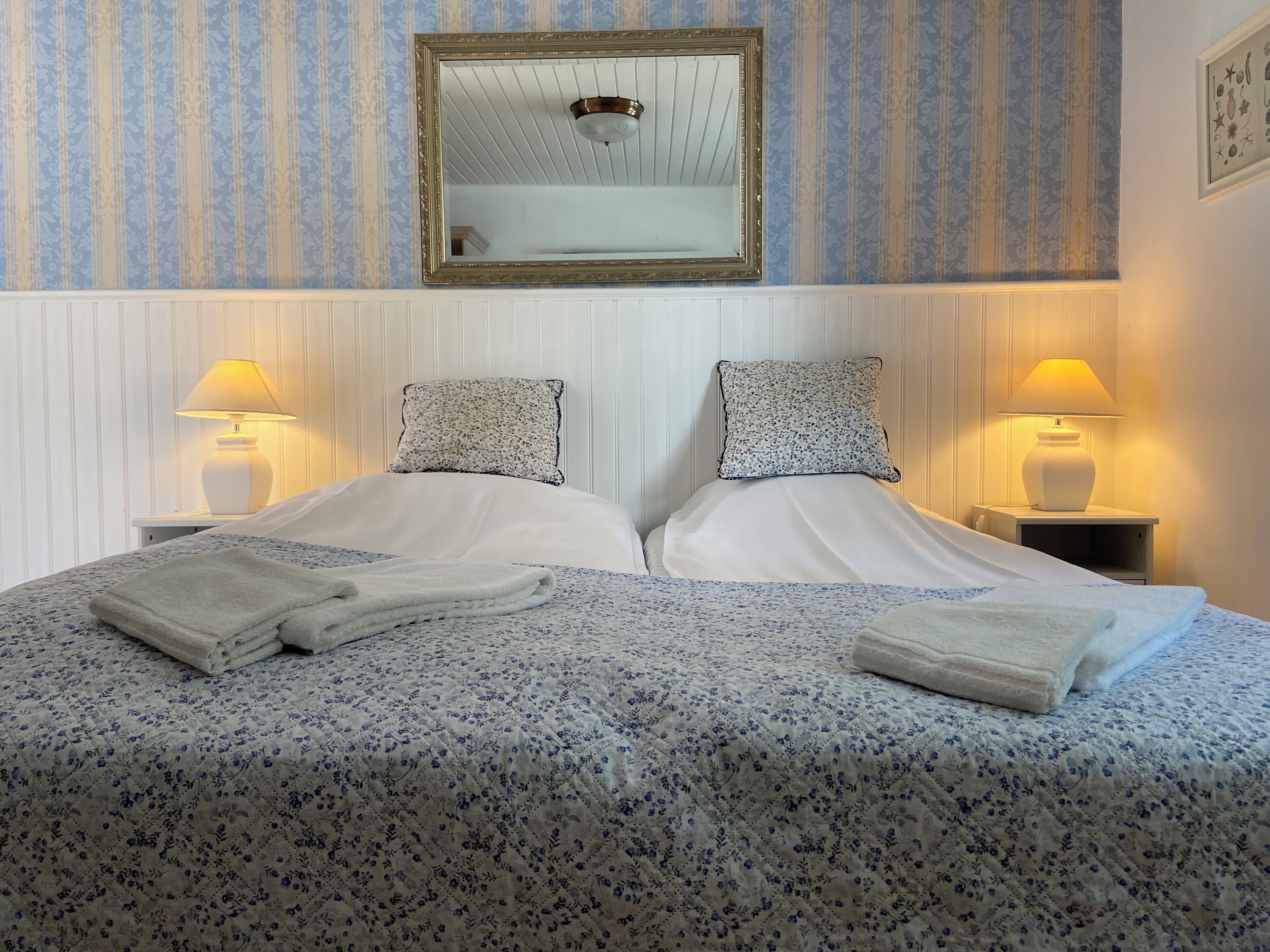 Una cama doble con ropa de cama floral, dos lámparas de noche y un espejo encima.