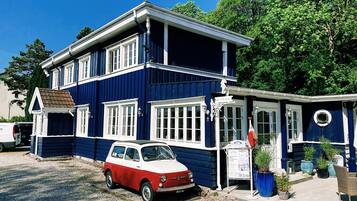 Un edificio de dos pisos con fachada azul y detalles blancos, con un coche clásico rojo y blanco estacionado frente a él.