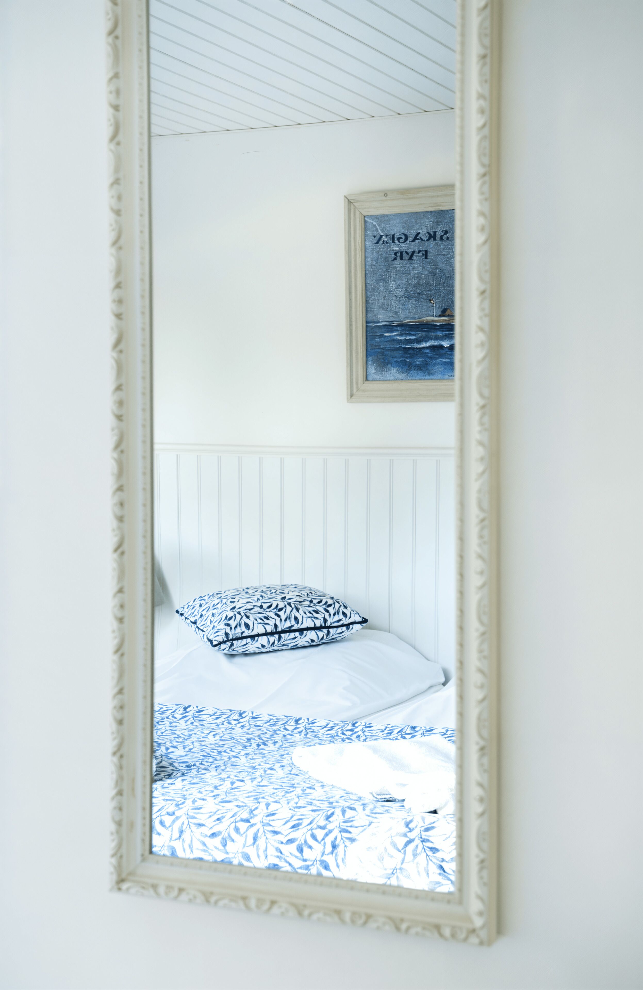 A bedroom with a bed, a framed picture on the wall, and a mirror reflecting the room.