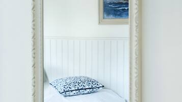 A bedroom with a bed, a framed picture on the wall, and a mirror reflecting the room.