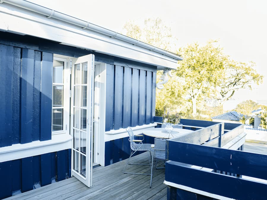 A deck with a table and chairs, a door, and a blue exterior wall.