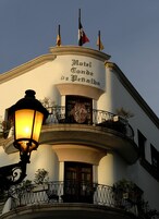 Un hotel con balcón, un reloj y banderas.