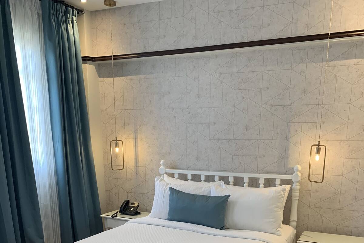 A neatly arranged bedroom with a large bed, a bedside table with a phone, and a hanging light fixture.