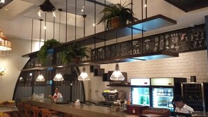 Un área de bar moderna con lámparas colgantes, una pizarra con el menú y un expositor refrigerado.