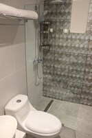 Un baño moderno con ducha envuelta en vidrio, inodoro blanco y pared con diseño de azulejos.