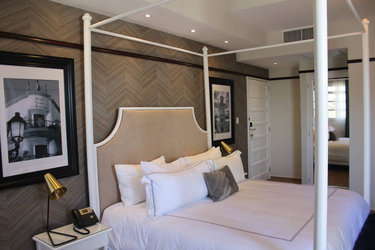 A four-poster bed with white linens, a bedside telephone, and a framed picture on the wall.
