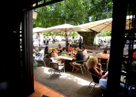 Un café al aire libre con mesas y sombrillas, rodeado de árboles.