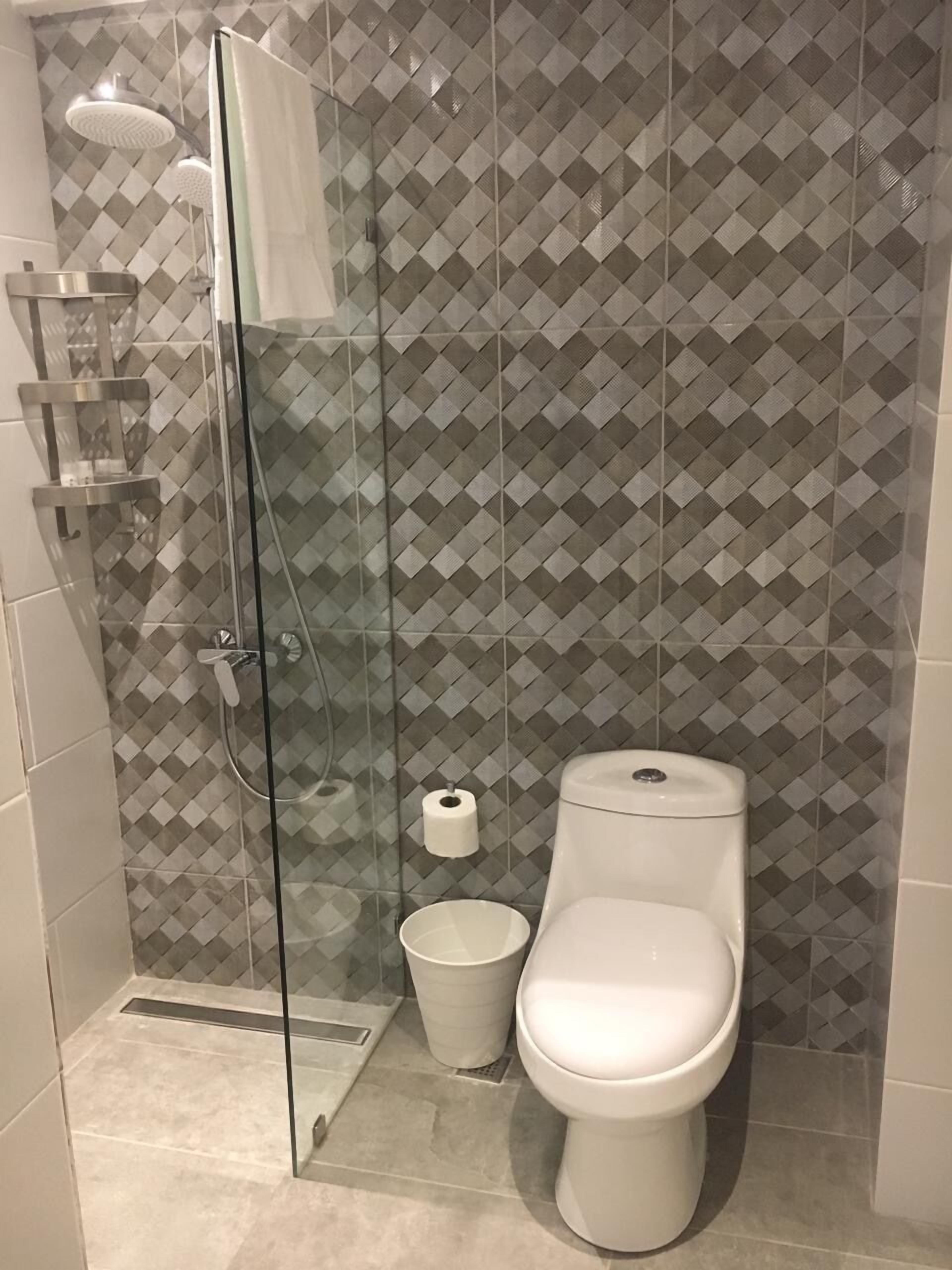 Casa de banho moderna com cabine de duche em vidro, sanita e um pequeno contentor de lixo.