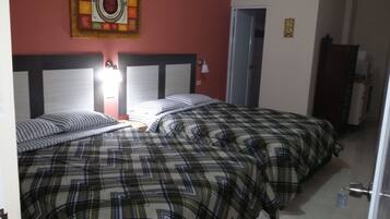Habitación de hotel con dos camas, cada una con colcha de cuadros, cabecero con panel decorativo y una obra de arte colgada en la pared sobre las camas.